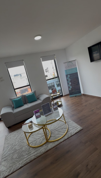 Sala de espera de Cortesia Medical Spa con sofá gris, mesas doradas y banner informativo